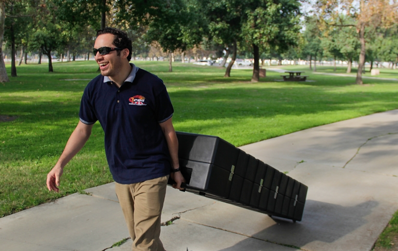 Human pulling a Rhino Roller Hard Case through the park while smiling and wearing sunglasses