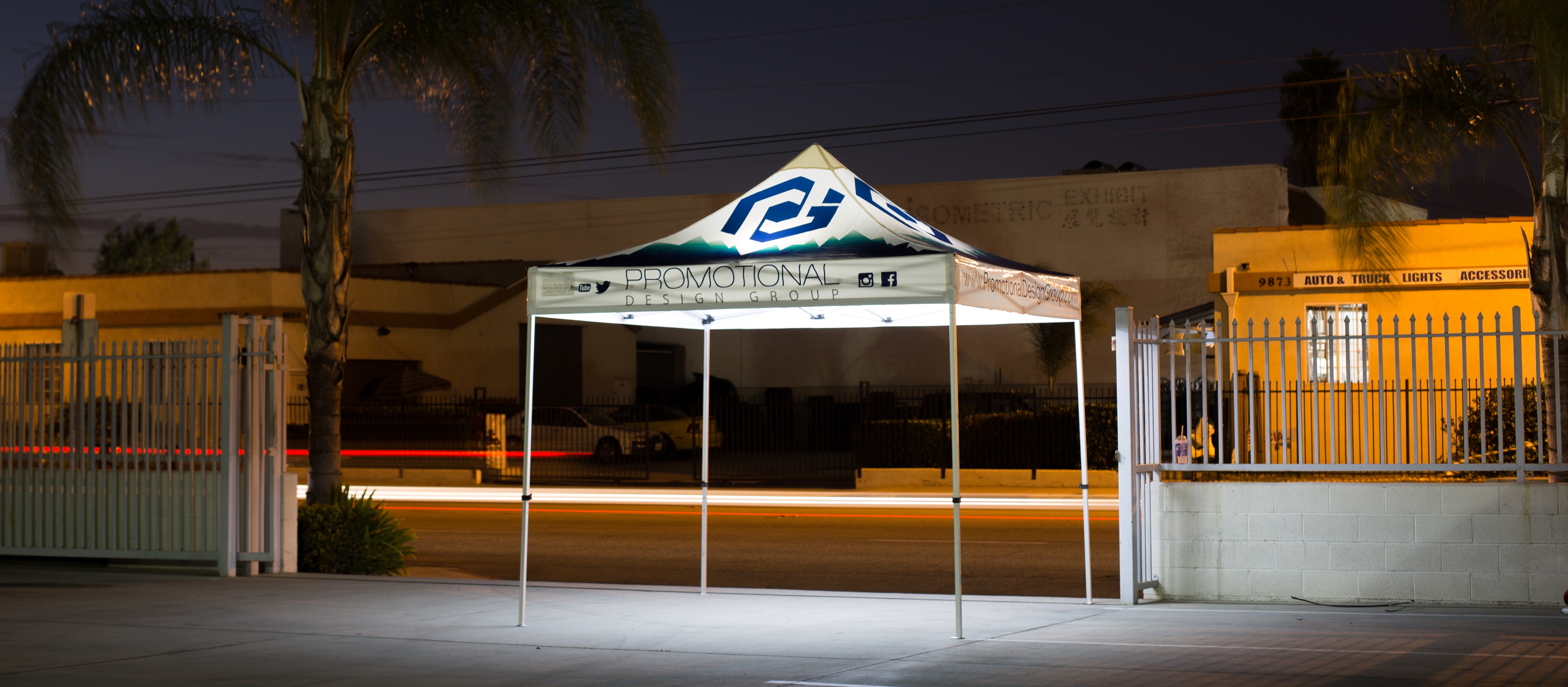 Canopy tent lights with a car passing in the background and an illuminated pop up canopy in the forefront