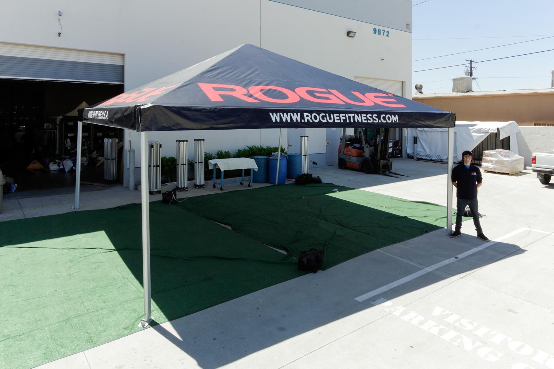Rogue Fitness 20x20 Standard Frame Tent with a printed tent top and a person standing next to it for size comparison