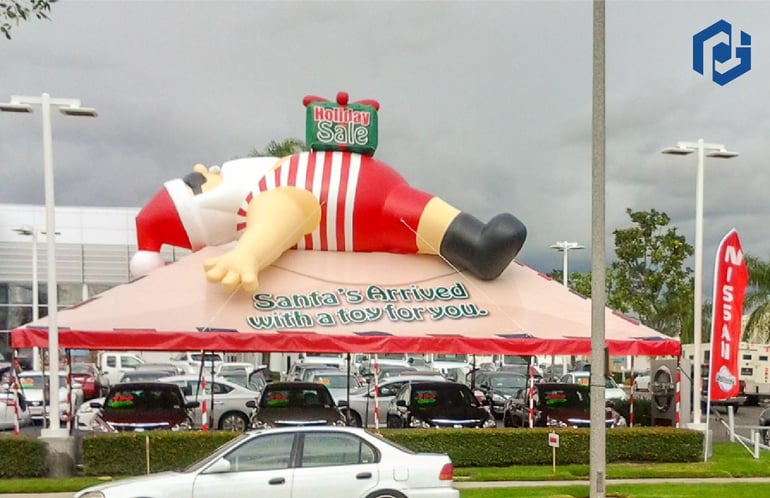Lazy Santa inflatable in a summer Swimsuit with a gift on his belly installed on top of a Christmas Tent