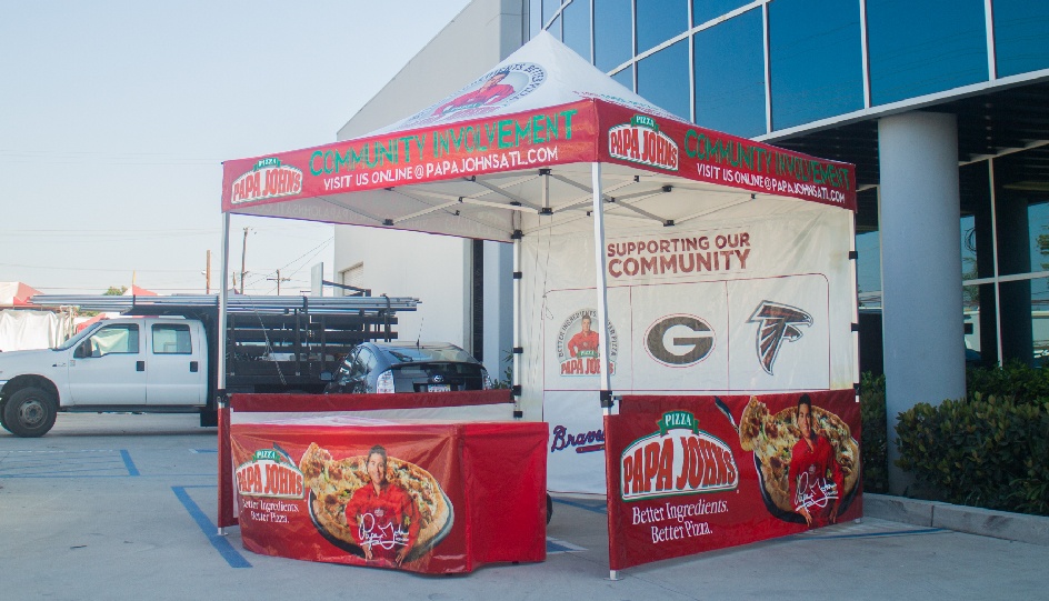 Papa Johns Gold canopy package with printed tent top, printed back wall, printed short walls and rail skirts, and printed table cover in front of business.