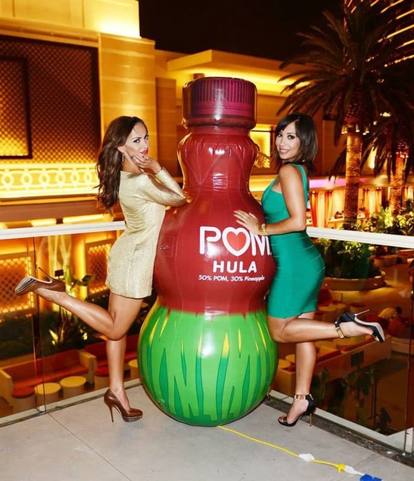 Large custom POM bottle inflatable replicas displayed with models to show scale for beverage promotions and branded events.