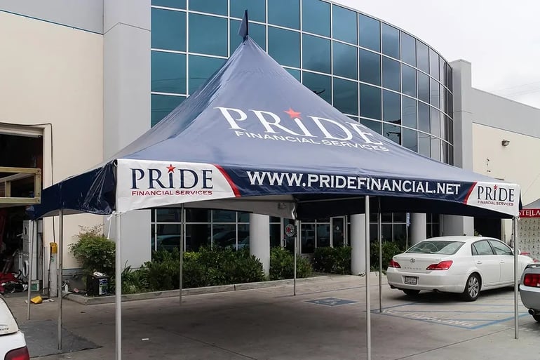 Angled view of a high peak event tent with Pride Financial Services roof logo and printed website valance