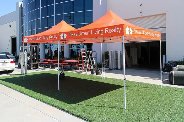 Orange branded pop up canopies with repeat valance text for real estate event marketing setup