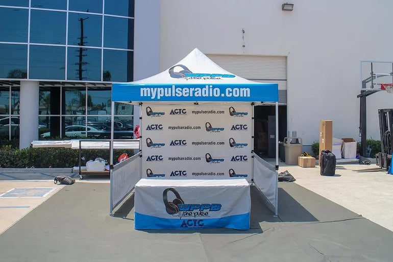 Branded pop up canopy booth with step-and-repeat back wall and printed table cover for events