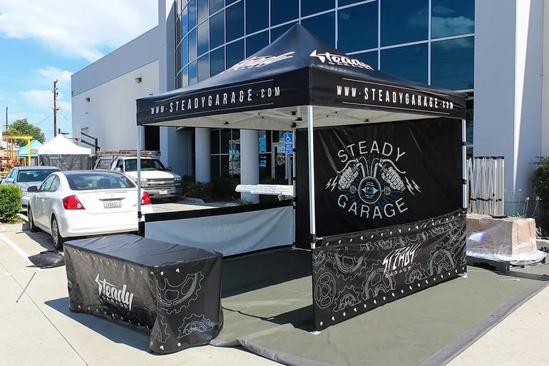Branded pop up canopy booth with Steady Garage back wall, printed rail skirts, and table cover