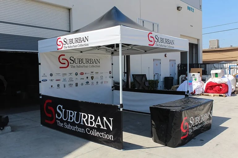 Custom pop up canopy booth with Suburban Collection branding, printed rail skirt, and back wall logos