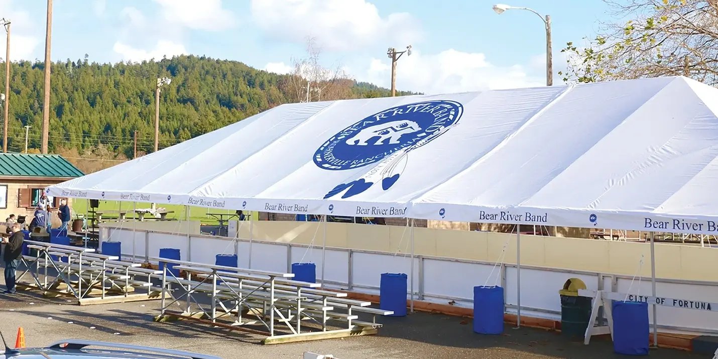 White frame tent covering a portable ice skating rink with bleachers for a seasonal event setup.