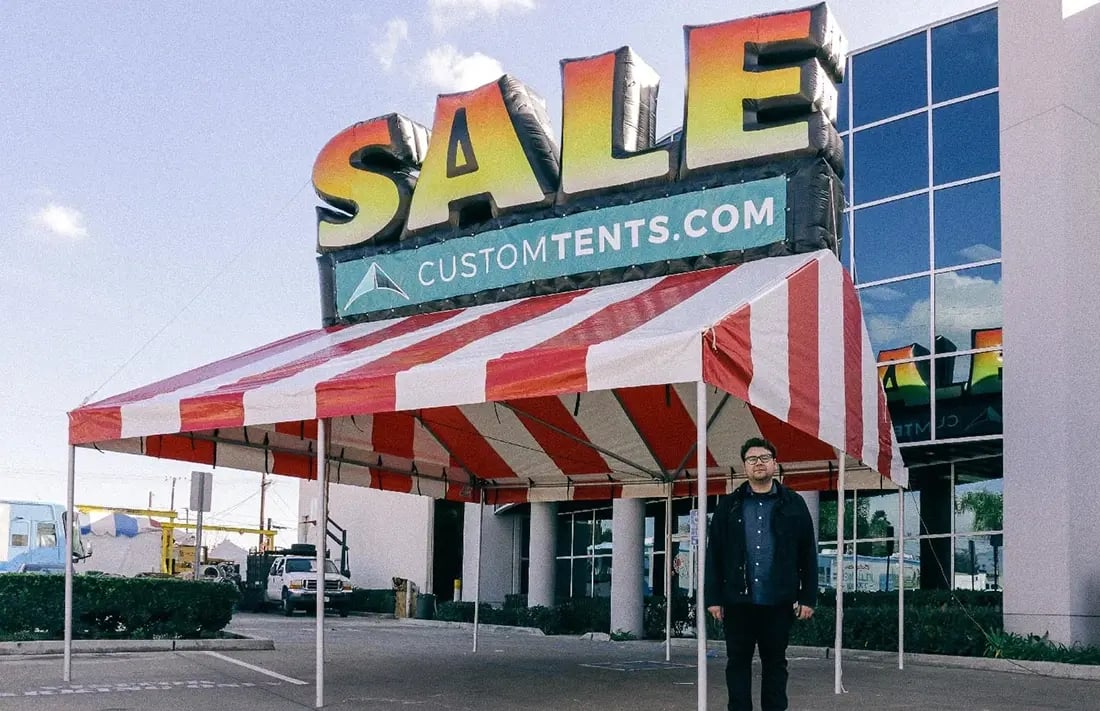 Gable frame tent with red-and-white striped top and SALE inflatable sign for event promotion.
