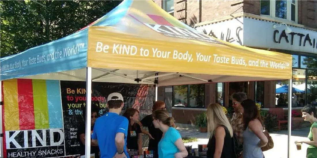 KIND Healthy Snacks branded pop up canopy at an outdoor event with people gathered at the booth