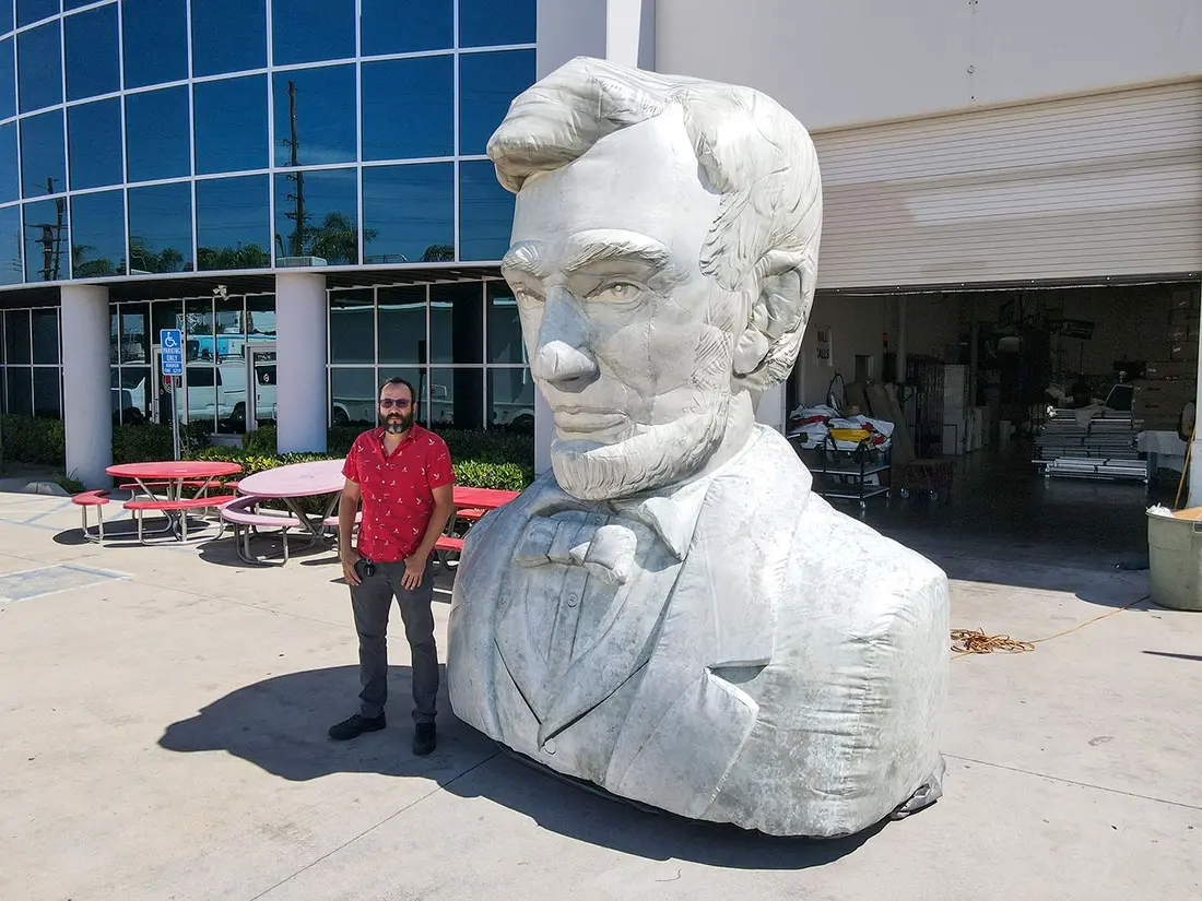 Inflatable Abraham Lincoln bust shown with a person for scale at an outdoor event setup Inflatable Abraham Lincoln bust shown with a person for scale at an outdoor event setup